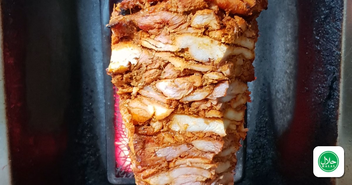 A vertical shawarma spit turning in front of a grill