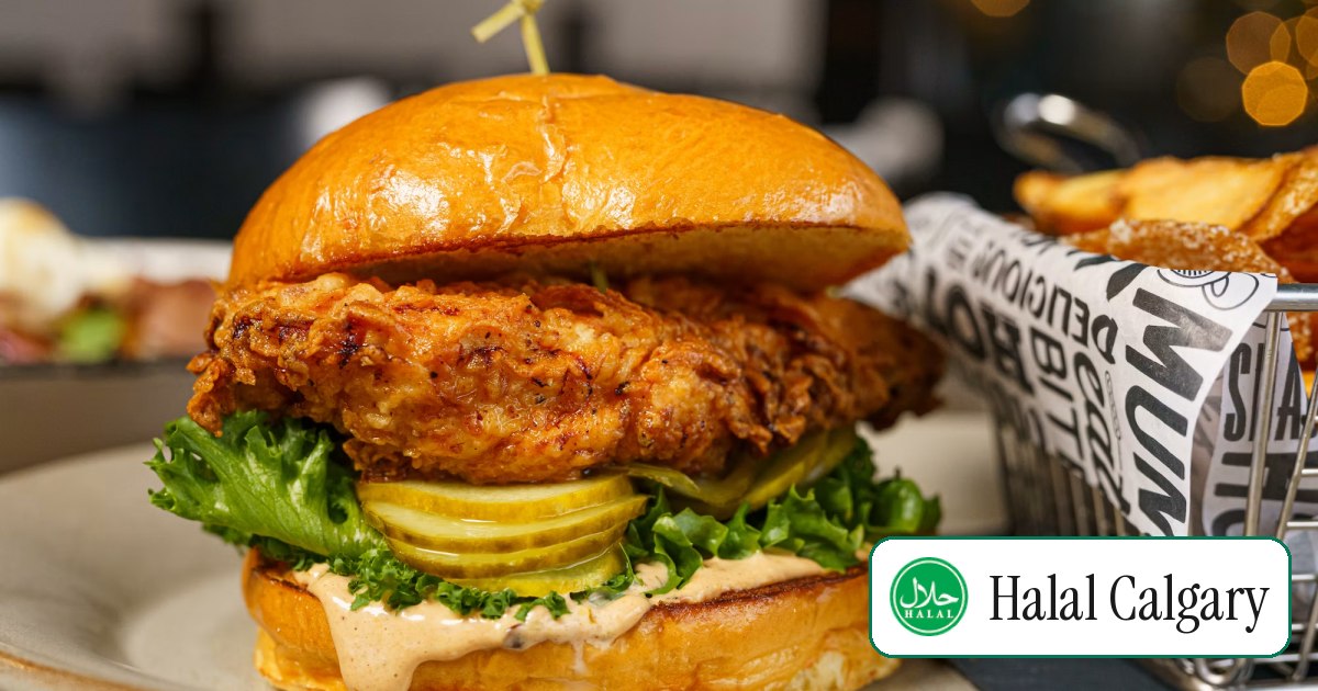 A hot chicken sandwich on a plate beside a basket of fries