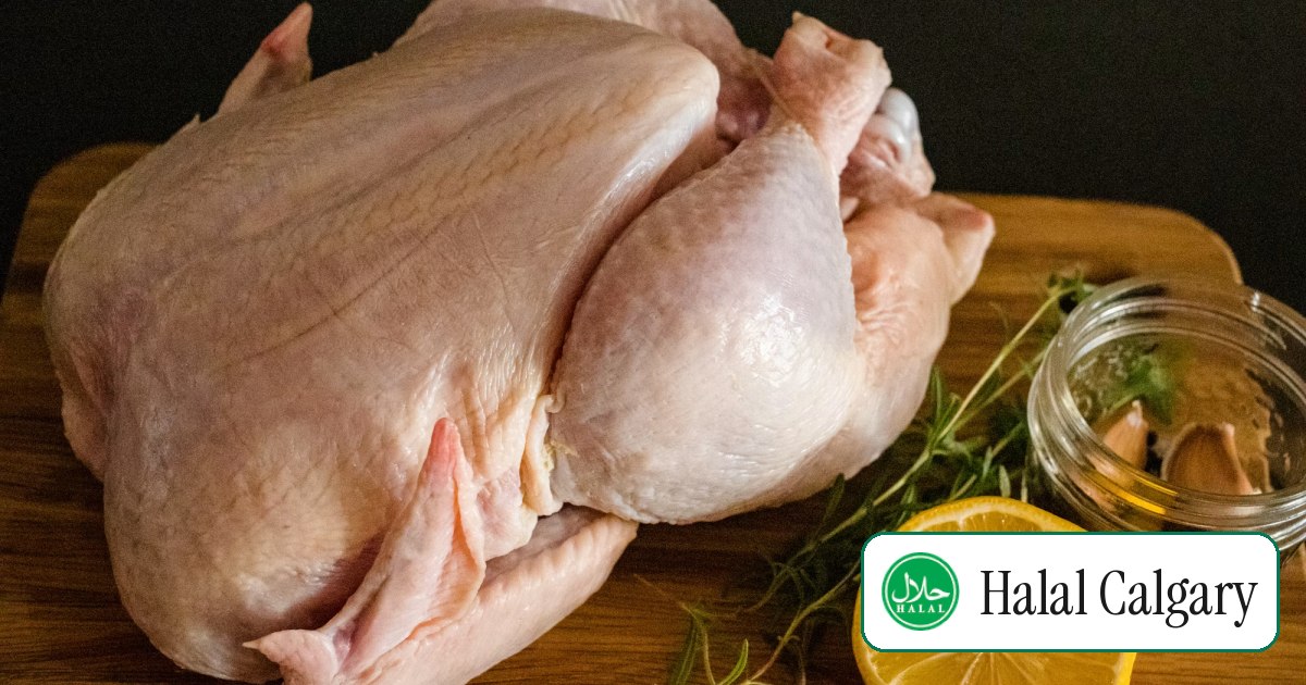 A whole raw chicken on a wooden cutting board with lemon and herbs